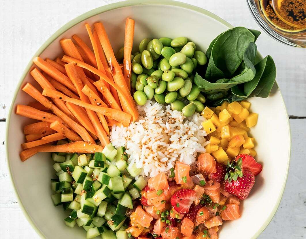 bol de poke au saumon carottes édamanes concombre fraises et riz dans un bol