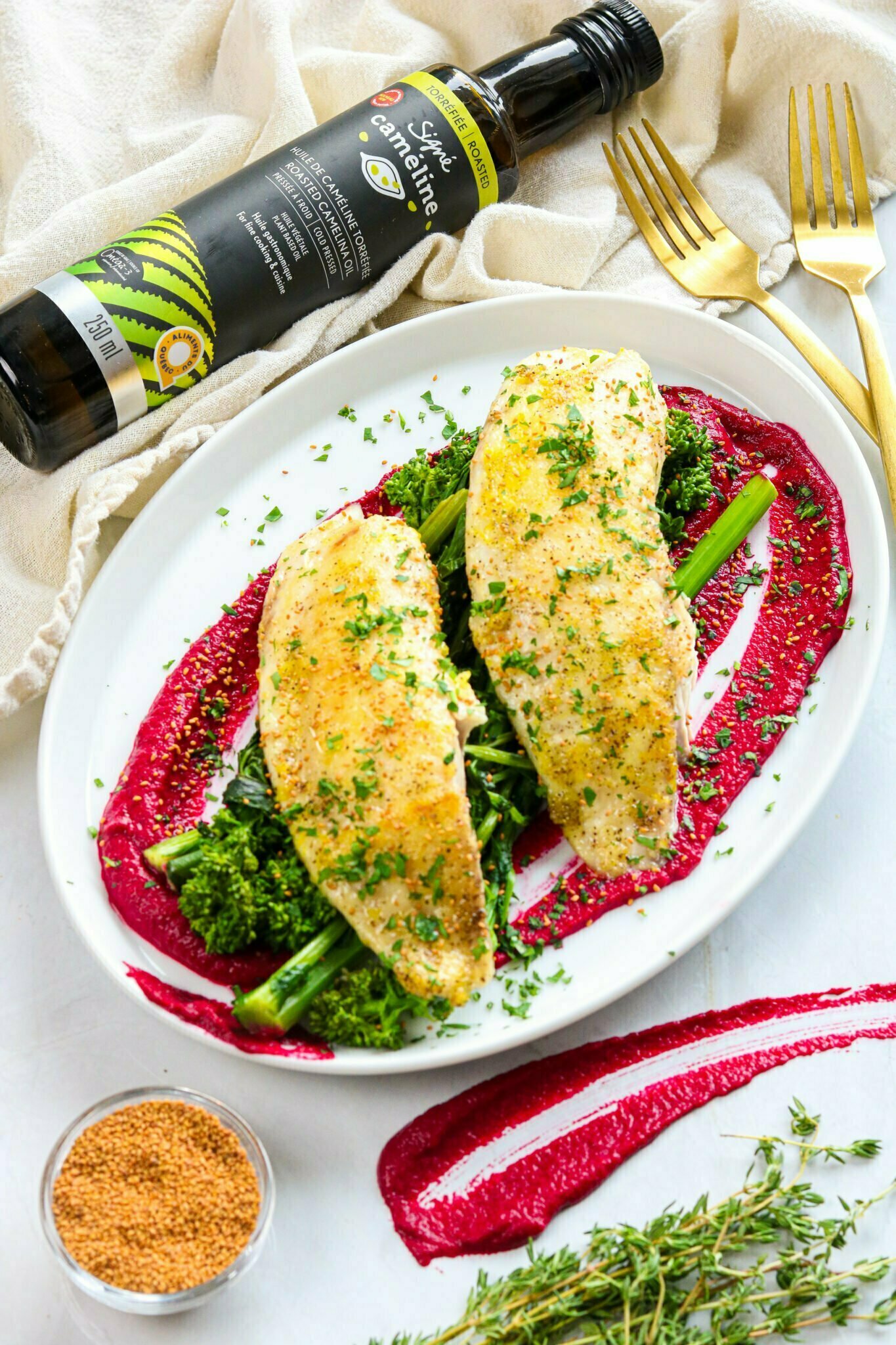 Poisson, broccoli et betterave dans une assiette avec une bouteille de caméline.